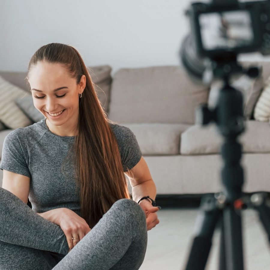 Doing lessons on camera. Young woman with slim body type and in yoga clothes is at home.