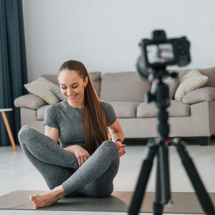 Doing lessons on camera. Young woman with slim body type and in yoga clothes is at home.